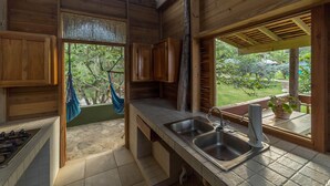 Een keuken met houten kasten, een stenen aanrecht, een spoelbak en uitzicht op een tuin door een raam.