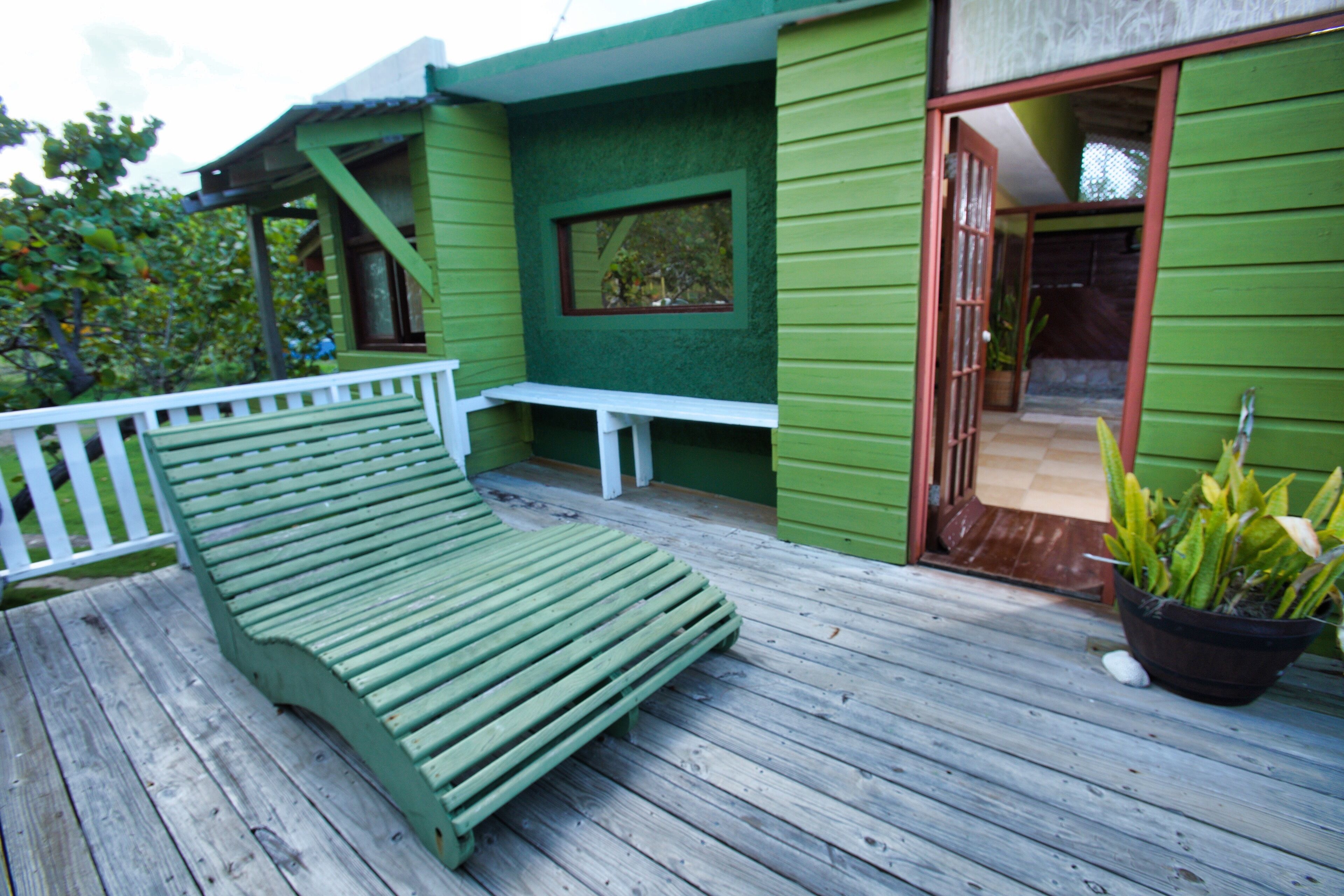 A green wooden deck with a bench and a potted plant.