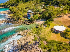 A coastal property with a house surrounded by trees, a beach, and rocky terrain.