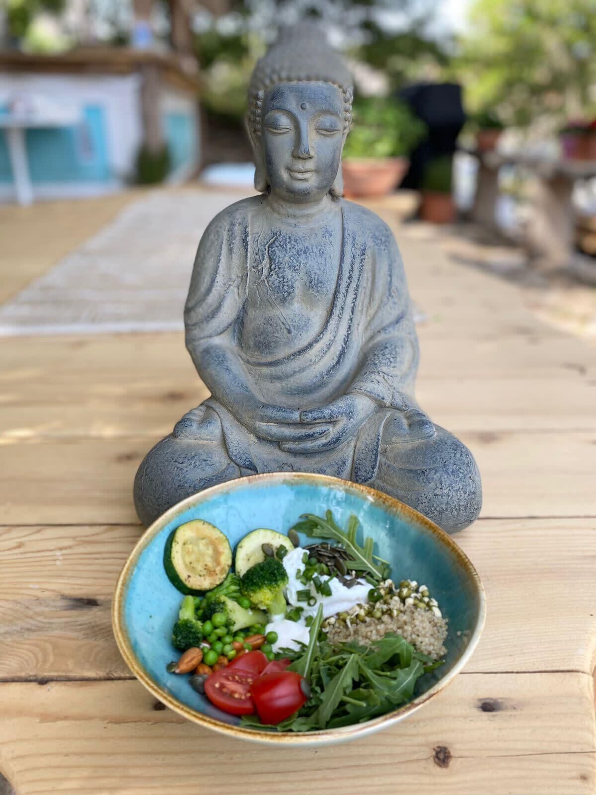 A Buddha statue on a wooden table with a bowl of salad in front.