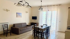 Ein Wohnzimmer mit Sofa, Esstisch, Stühlen und einem Fernseher.