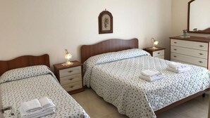Ein Schlafzimmer mit zwei Betten, hölzernen Kopfteilen, Nachttischen mit Lampen, einer Kommode und einem Spiegel.