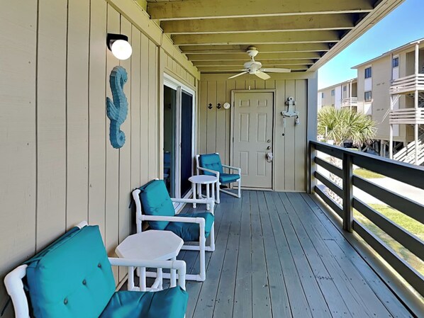 A covered porch with white furniture, a ceiling fan, and a view of the ocean.