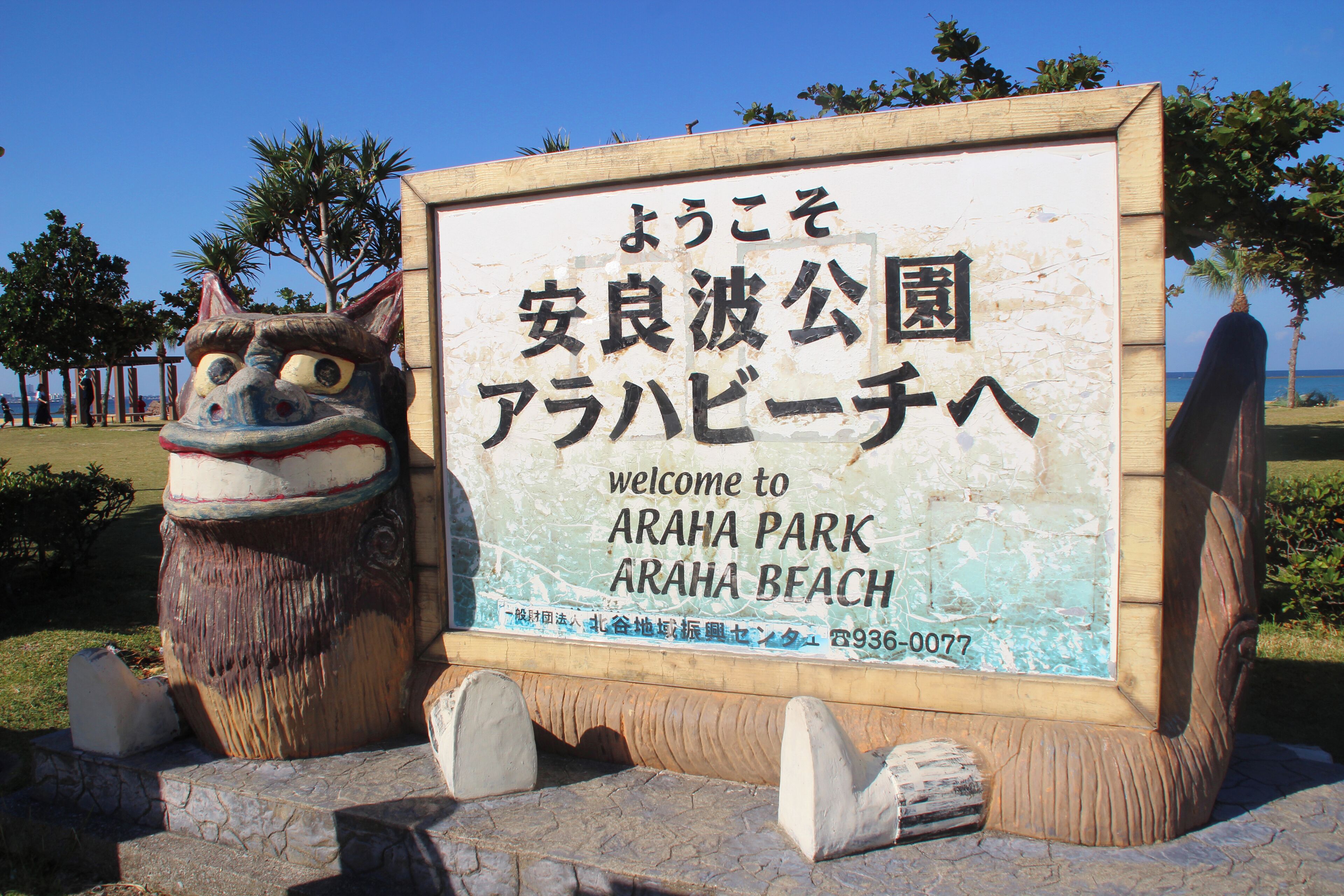 A welcome sign for ARAHA PARK at ARAHA BEACH with Japanese text and a large decorative sculpture.