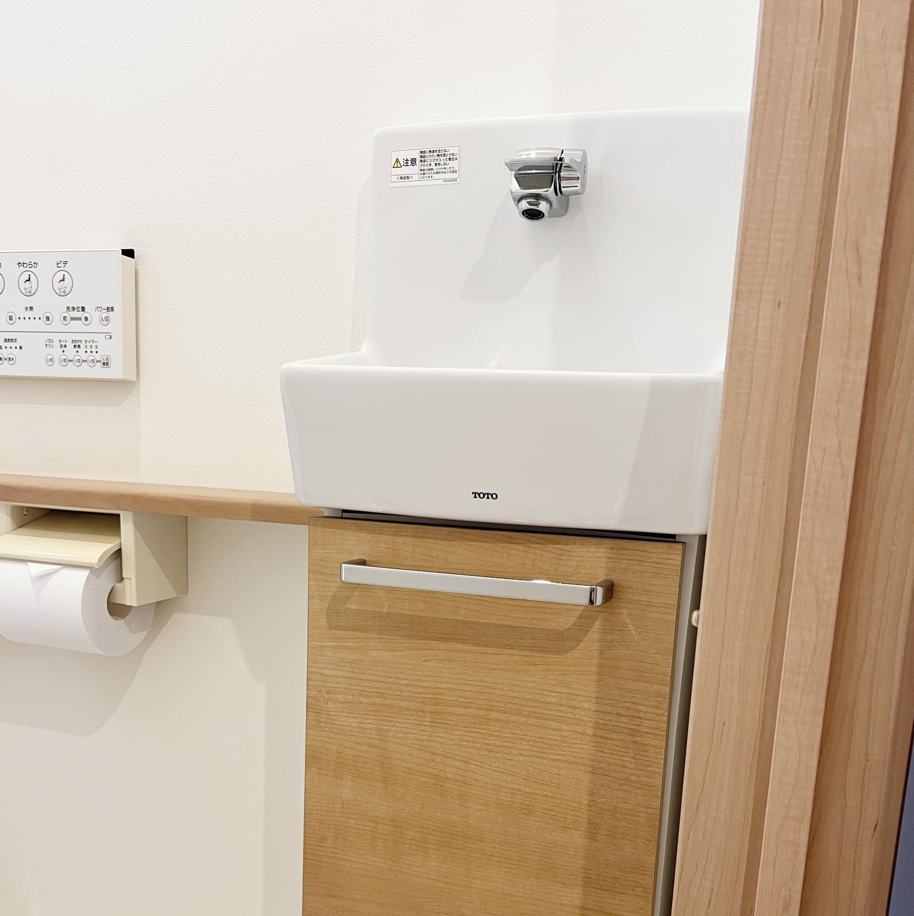A white toilet with a TOTO brand label, a wooden cabinet below, and a toilet paper holder to the left.
