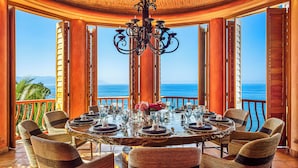 A round dining table with chairs, set for a meal, overlooking a scenic ocean view. - Villa Estrella Mar - 5 Star Luxury Villa - Staff - Private Pool - On the beach! (Puerto Vallarta)