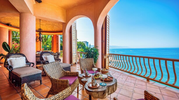 A balcony with wicker furniture, a dining table with plates, and a view of the sea. - Villa Estrella Mar - 5 Star Luxury Villa - Staff - Private Pool - On the beach! (Puerto Vallarta)