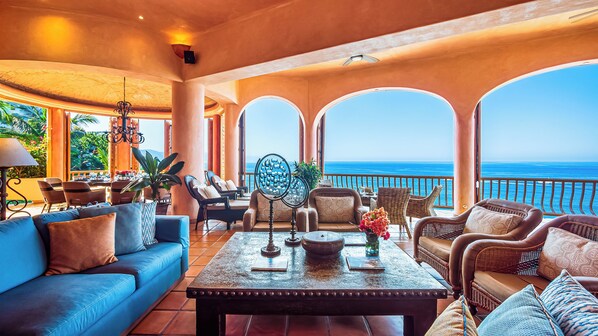 Amplia sala de estar con vista al océano, amoblada con sofás, sillones y una mesa de centro.
