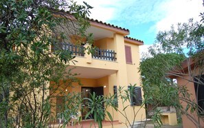 Um edifício de dois andares com varanda, rodeado por vegetação.