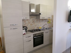 Uma cozinha moderna com armários claros, fogão a gás, forno e pia.