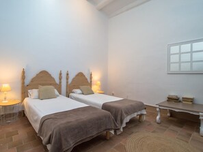 Two single beds with wooden headboards and white mattresses, flanked by nightstands and a small table with a chair.