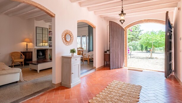 A spacious living room with a fireplace, a large mirror, and a view of the garden through an open archway. - Costabravaforrent Tallada (La Tallada d'Empordà)