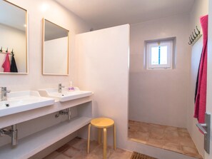 Bathroom features two sinks with separate faucets, a shower area with a glass door, and a window above.