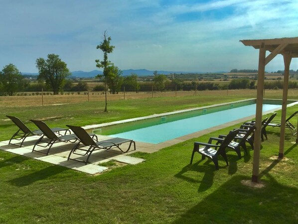 Relax by the serene pool surrounded by a tranquil landscape and shaded by a pergola.