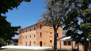 Un edificio grande de varios pisos con techo plano y ventanas arqueadas, rodeado de césped y árboles.