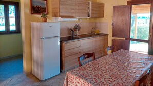 Cocina compacta con armarios de madera, un refrigerador blanco y una mesa de comedor con mantel floral.