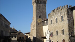 A historic stone tower with a clock, flags, and a statue in a town square. - Basic two-room apartment in the city center with kitchen and private parking (AREZZO)