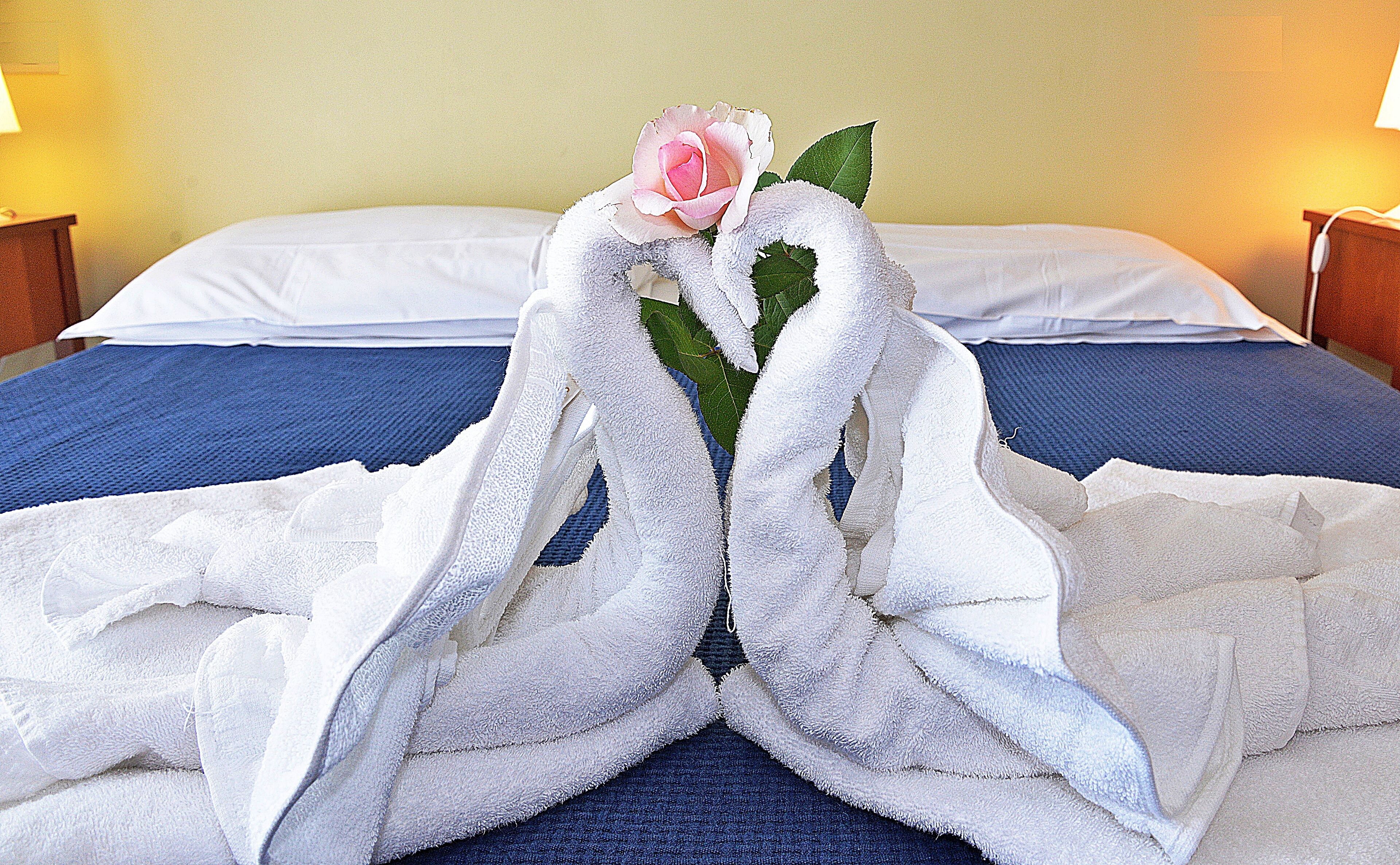 A bed with white sheets, a blue blanket, and a rose in the center.