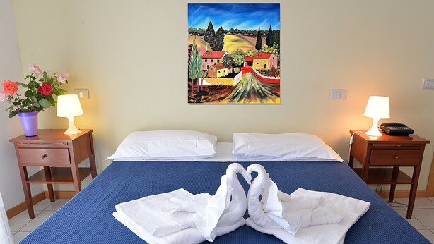 A hotel room with a bed, two bedside tables, a painting on the wall, and a potted plant. - Basic two-room apartment in the city center with kitchen and private parking (AREZZO)