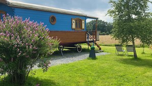 Una casa flotante azul y marrón con terraza y ventanas, rodeada de hierba verde y árboles.