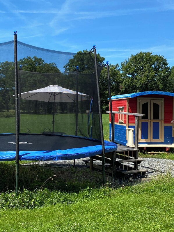 A trampoline with a safety net and a small pavilion with a blue roof.