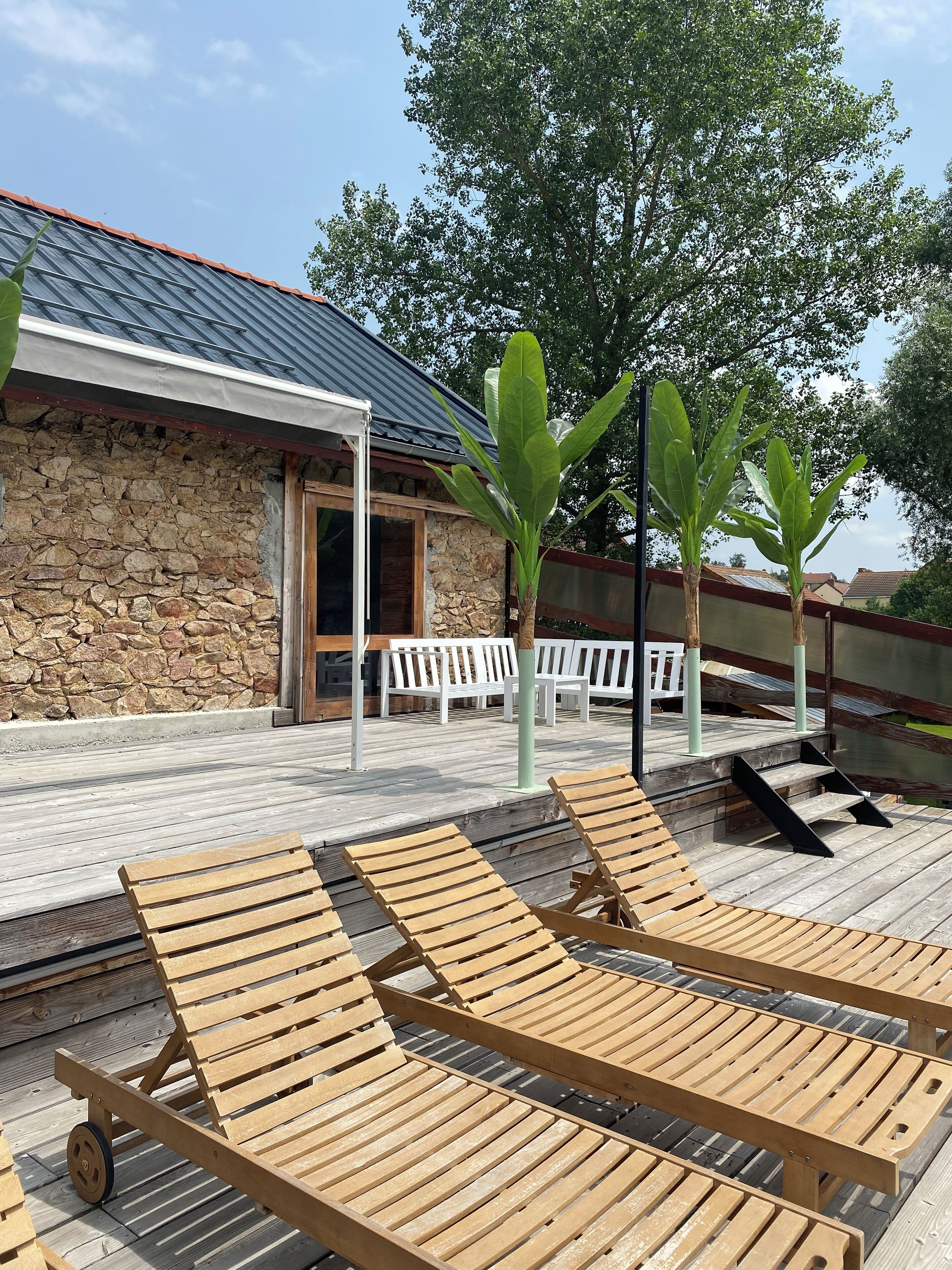 A wooden deck with lounge chairs, a stone wall, and a metal roof.