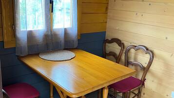 A wooden dining room with a table and chairs, a window with curtains, and a view of greenery outside.
