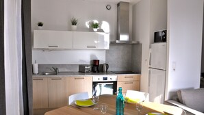 Moderni keittiö, jossa on valkoiset kaapit, sisäänrakennettu uuni ja mikroaaltouuni. Keittiössä on ruokapöytä tuoleineen sekä vesipullo.