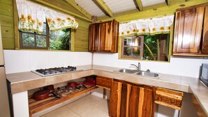 A kitchen with wooden cabinets, a gas stove, a sink, and a window with a sunflower curtain. -  Amazingly Affordable Savings "Rustic Jamaican Vibes" on Ocean Front, Selecluded (St. Mary, Jamaica)