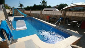 Piscina com escorregador, escada e área de estar com cadeiras e mesa.