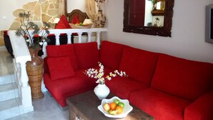 Una sala de estar con un sofá rojo, un florero blanco con flores y un frutero sobre una mesa de madera.