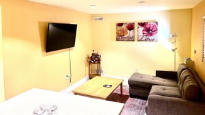Una sala de estar con una televisión de pantalla plana, un sofá, una mesa de centro y dos cuadros florales.
