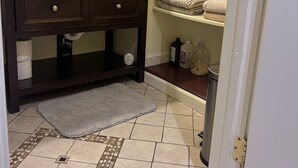 Un baño con tocador de madera oscura, suelo de baldosas con diseño geométrico, una puerta blanca y estantes con toallas dobladas.