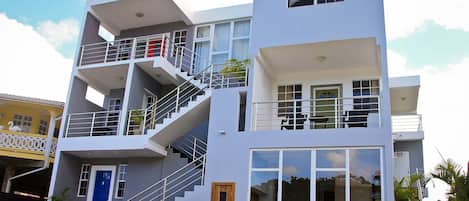 A modern multi-story building with a blue door, white walls, and a balcony with a railing.