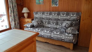 Una habitación acogedora con un sofá estampado, paredes de madera, un pequeño armario de madera y una ventana con cortinas.
