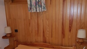 Habitación con paneles de madera, una cama, dos mesitas de noche con lámparas y un cortinaje floral.