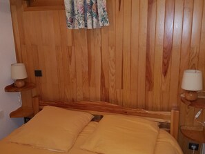 Habitación con paneles de madera, una cama, dos mesitas de noche con lámparas y un cortinaje floral.