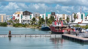 A waterfront marina with boats docked, a pier, and colorful buildings in the background. - Locastudio "Pomme Kanel (Sainte-Anne)