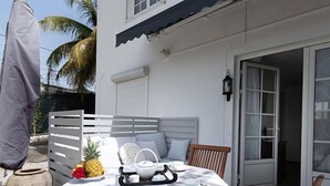 A patio table set with a white tablecloth, a pineapple, and a small decorative item. - Locastudio "Pomme Kanel (Sainte-Anne)