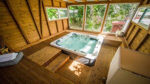 A wooden deck with a hot tub, wooden walls, and large windows overlooking greenery. - Locastudio "Pomme Kanel (Sainte-Anne)