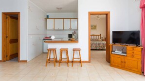 A compact living space with a kitchenette, a dining area with stools, a TV, and a bedroom with a bed and curtains. - Sunny 2-Bedrooms With Large Terrace. WiFi (Arona)