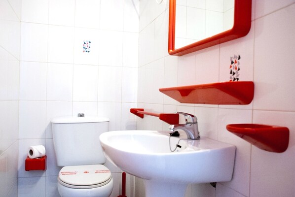 Een badkamer met een wit toilet, een witte wastafel en een rode spiegel.