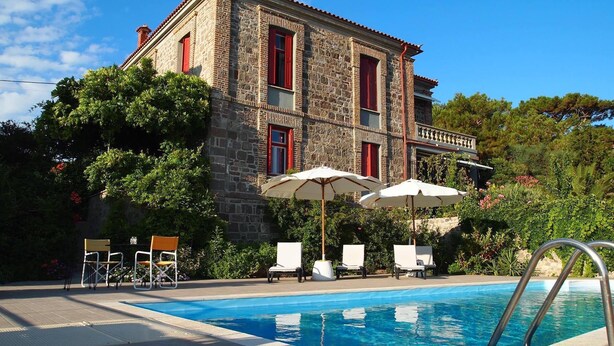 A stone building with a swimming pool, outdoor seating, and red shutters.