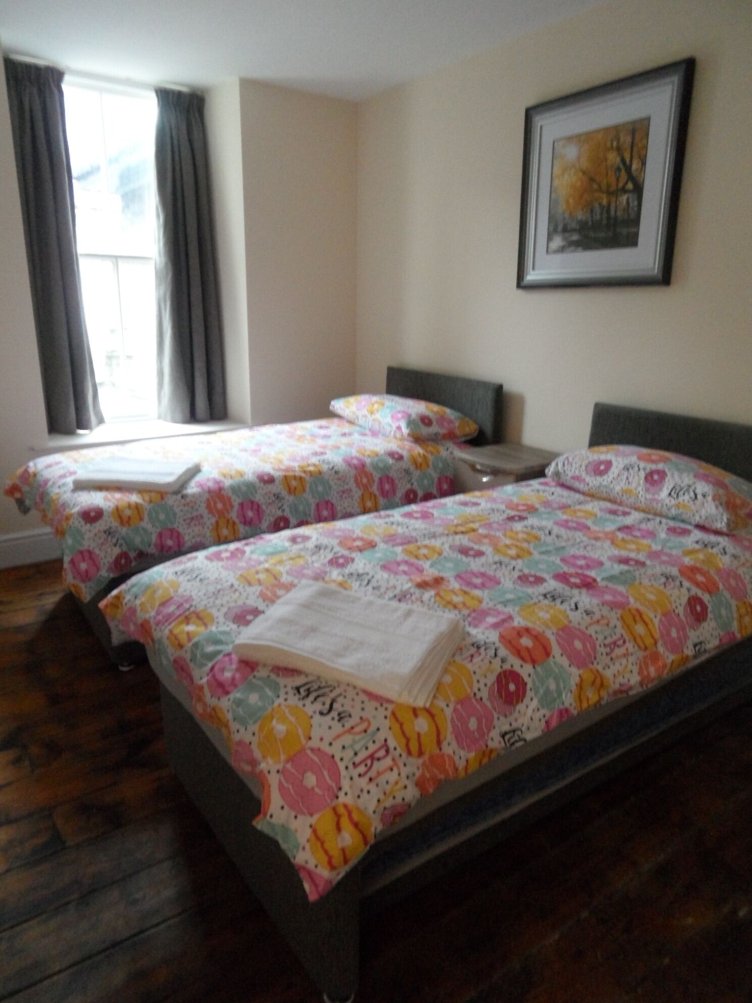 Una habitación con dos camas, cada una con ropa de cama estampada con motivos florales y una almohada. Hay un cuadro en la pared y una ventana con cortinas.