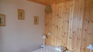 Quarto com paredes de madeira, cama com roupa de cama floral, duas mesas de cabeceira com luminárias e duas imagens emolduradas na parede.