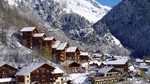 Un chalet de montagne composé de plusieurs bâtiments en bois, avec un télésiège et des montagnes enneigées en arrière-plan.