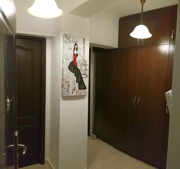 A hallway with a dark wooden wardrobe, a door, and a wall-mounted artwork depicting a fashion model with the text "Salon de Mode Paris".