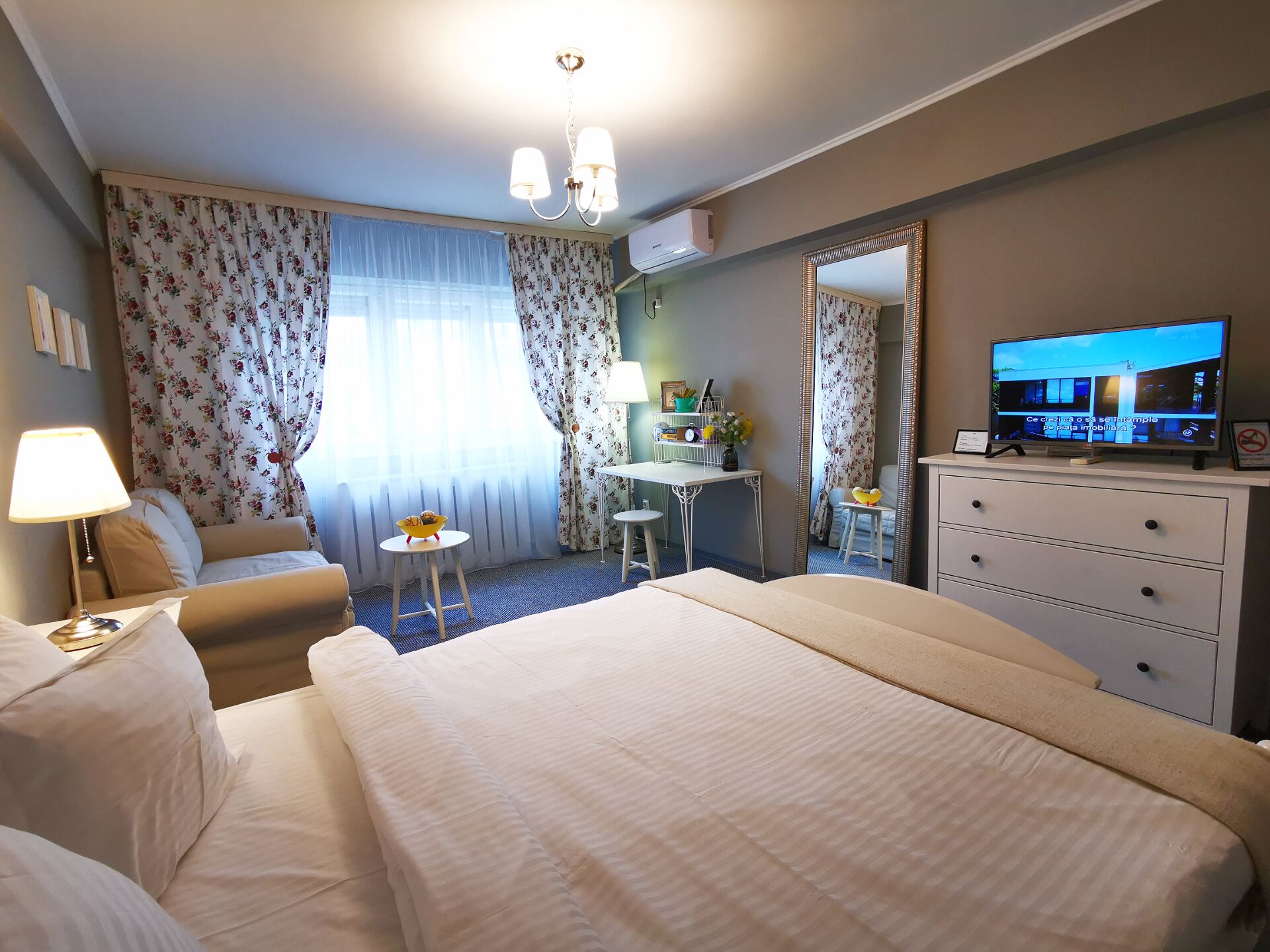 Ein Hotelzimmer mit einem großen Bett, einem Schreibtisch, einem Sessel, einem Fernseher und einem Spiegel.