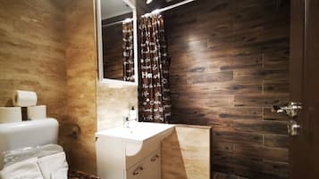 Un baño con pared de madera, un lavamanos blanco, un espejo y una cortina de ducha con texto.