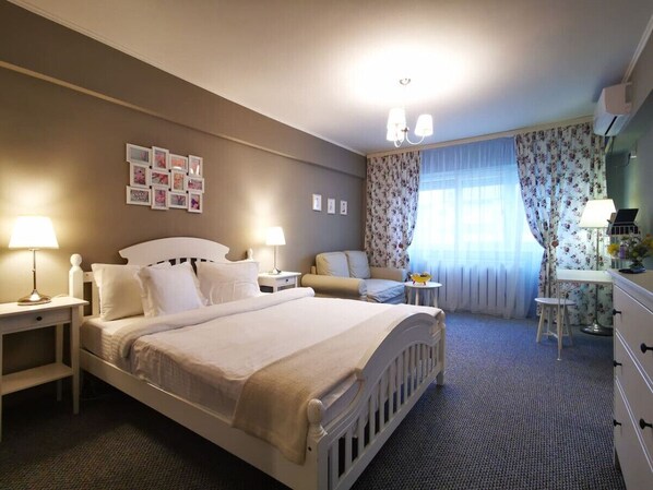 Ein Hotelzimmer mit einem großen Bett, zwei Nachttischen mit Lampen, einem Schreibtisch mit Stuhl, einem Schminktisch und einem Fenster mit blumigen Vorhängen.